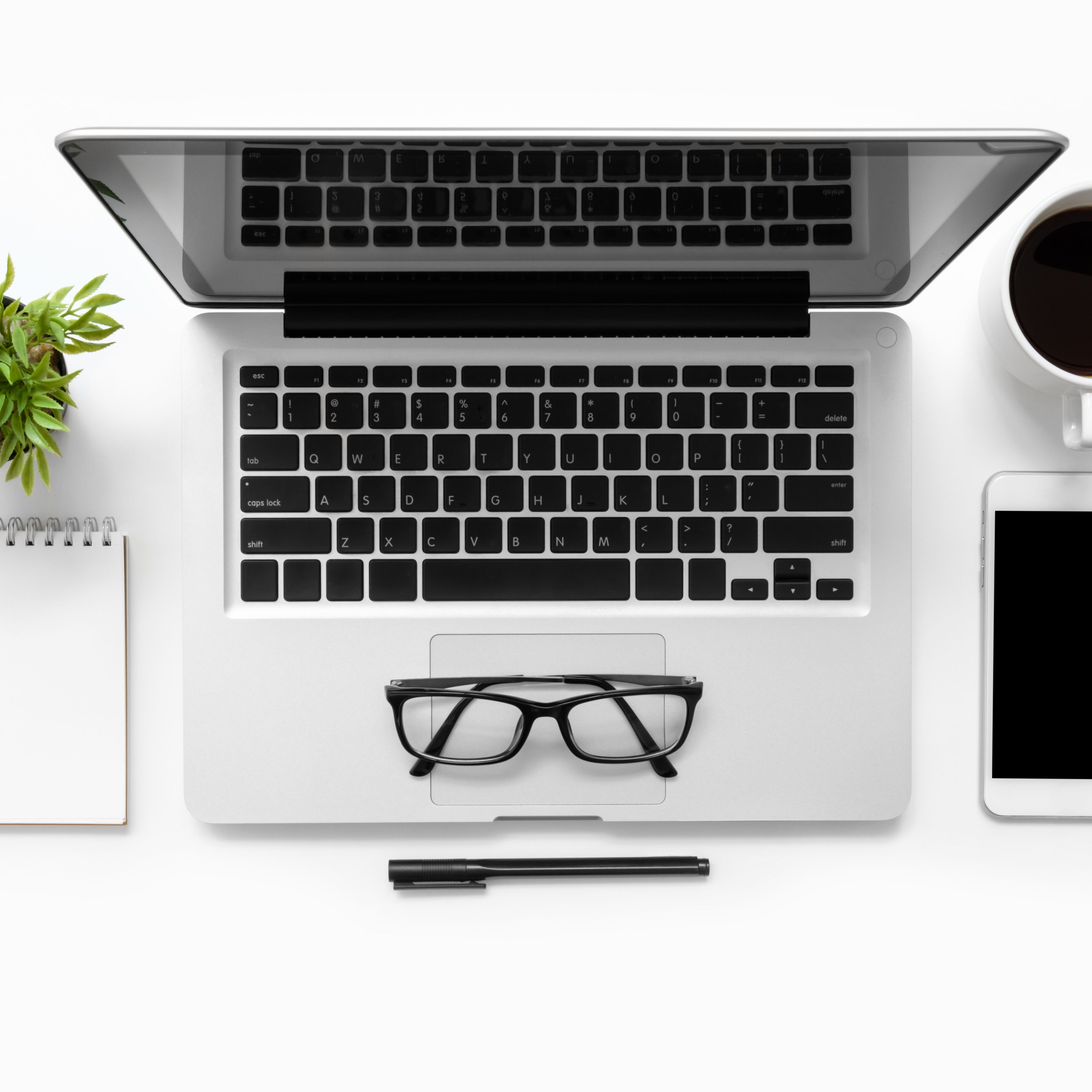 White office desk table with laptop computer, smartphone, cup of coffee, notebook and supplies. Top view, flat lay.